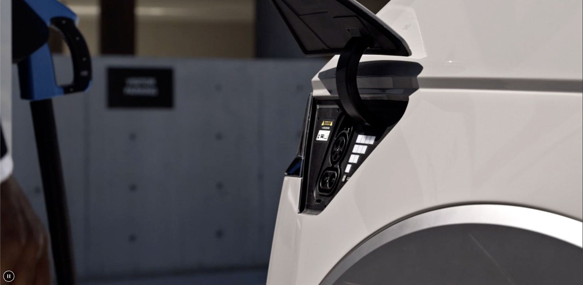 Charging port of a white electric vehicle with the charger nozzle visible on the left.