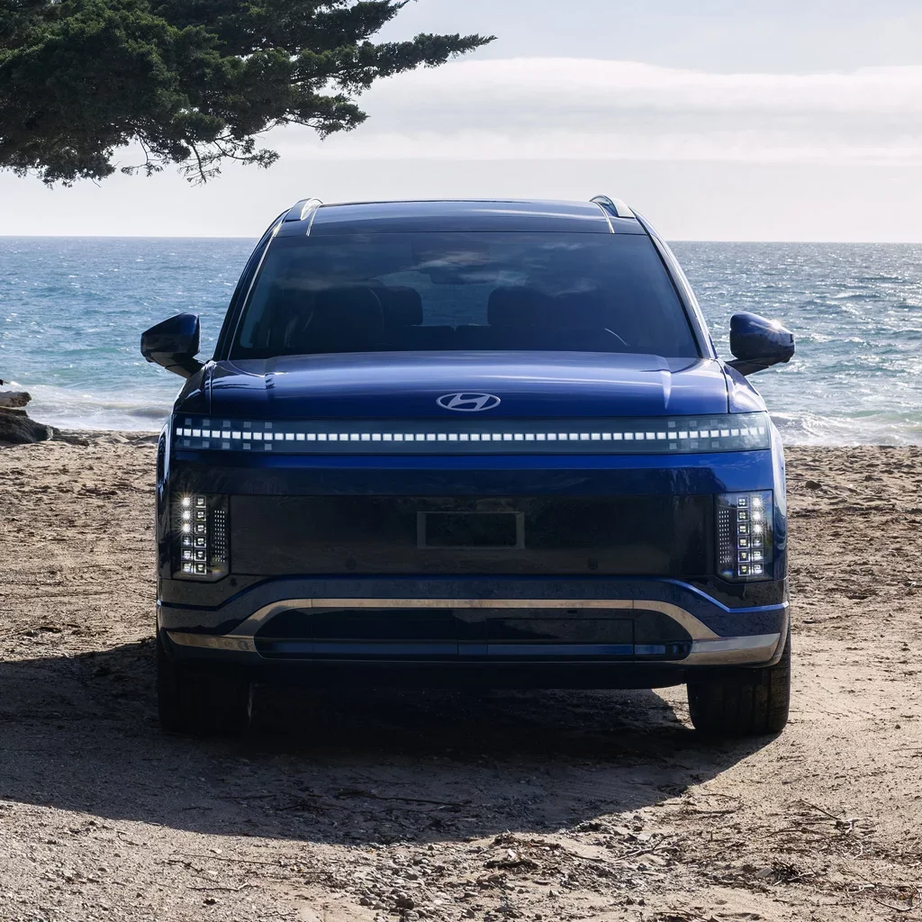 Front view of a blue Hyundai Ioniq 5 electric car on a sandy beach with the ocean and sky in the background.