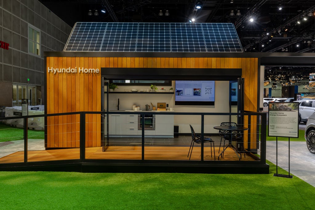 A small Hyundai Home structure with solar panels on the roof, a kitchen visible inside, and a small porch with a table and chairs.