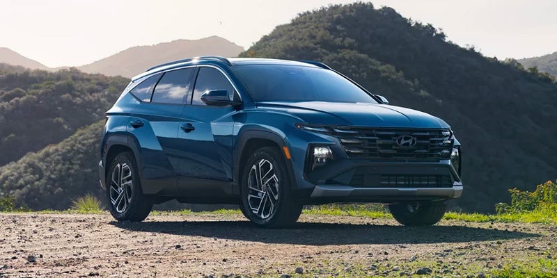 Blue Hyundai Tucson SUV parked on a gravel roadside with green mountains